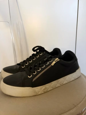 Svarta sneakers  - Snygga svarta sneakers med vita sulor och cool dragkedjedetalj på sidan. Knappt använda skor (använda några gånger) inga täcken på användning förutom lite smutts där nere. 