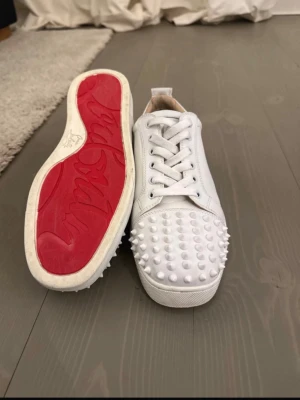 Vita Louboutin sneakers med nitar - Säljer ett par vita sneakers från Christian Louboutin, Perfekta för dig som vill sticka ut med en lyxig och edgy stil. Hör av dig vid fler frågor eller bilder! Och kom gärna med pris förslag!💕💕💕