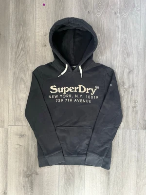 Svart hoodie från Superdry - Svart hoodie från Superdry med stor vit logga och text på bröstet🤩 Tvär fet och inga fel på hoodien passar S-Xs🙌🏻  Hör av er vid funderingar samt snabbaffär😇