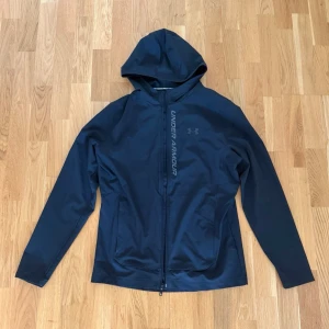 Svart Jacka från Under Armour - Snygg svart tunn jacka från Under Armour med dragkedja framtill och stor logga längs bröstet. Tillverkad i ett mjukt och stretchigt material som passar perfekt till träning eller chill. Utrustad med huva och två sidofickor för extra funktion. Pris kan diskuteras 