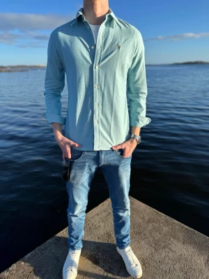 Ljusblå skjorta från Ralph Lauren - Snygg ljusblå skjorta från Ralph Lauren med klassisk krage och knappar framtill. Skjortan har lång ärm och den ikoniska broderade loggan på bröstet. Perfekt till jeans eller chinos för en clean och stilren look.Storlek S , 349kr