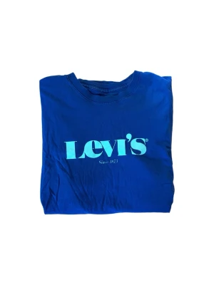 Blå Levi's t-shirt med logga - Snygg blå t-shirt från Levi's med stor turkos logga på bröstet. Klassisk rund halsringning och korta ärmar. Tillverkad i mjuk bomull som känns skön mot huden. Perfekt för dig som gillar enkel men stilren streetwear.