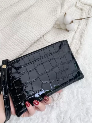 Svart plånbok i krokopräglat skinn - Stilren svart plånbok med glansig krokopräglad yta och handledsrem. Plånboken har ett elegant och modernt uttryck, perfekt för dig som gillar trendiga accessoarer. Praktisk storlek för att få plats med kort, cash och mobilen.