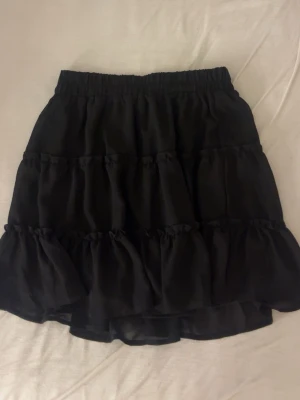 Svart volangkjol - Säljer ensvart kjol med volanglager. Man kan både ha den som en högmidjad och lågmidjad kjol. Aldrig använd då den var för liten för mig i midjan