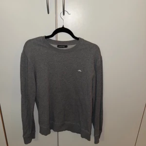 Grå sweatshirt från J.Lindeberg - En stilren grå sweatshirt från J.Lindeberg med rund halsringning och diskret logga på bröstet. Tröjan har långa ärmar och ribbade muddar vid ärmslut och nederkant. Perfekt för en avslappnad look.