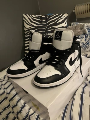 Air Jordan 1 Panda Black White High - Snygga Air Jordan 1 sneakers i svart och vitt, klassisk high-top modell med svart Swoosh och vita detaljer. Skorna har svart läder och vita paneler, samt ikoniska Jordan-loggor på sidan och plösen. Perfekta för dig som vill ha en stilren och tidlös look. Använt 2 gånger när jag skulle flyga sen dess har jag inte använt och det var i februari och jag köpte dom tidig februari. Kan diskutera pris