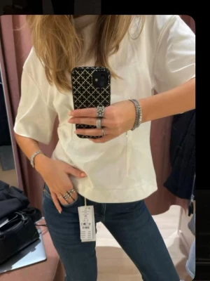 Vit t-shirt med intagen midja - Säljer en vit oversized t-shirt från med klassisk rund hals och intagen midja. T-shirten är i mjuk bomull och har en clean, minimalistisk look som passar till allt. Perfekt basplagg för alla tillfällen.