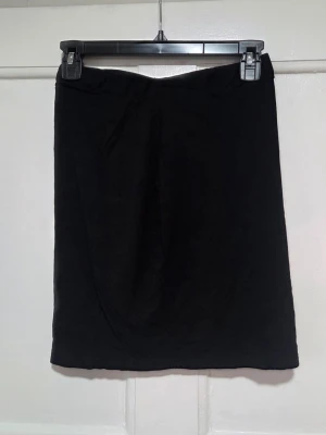 Svart pennkjol i mjukt tyg - En klassisk svart pennkjol med rak passform och enkel midja. Kjolen är kort med en längd på ca 43,5 cm och sydd i ett mjukt, följsamt tyg som ger en stilren look. Perfekt att matcha med crop tops eller oversized tröjor för en trendig outfit. Aldrig använd, den har bara legat i lådan hela tiden.