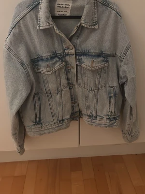 Ljusblå jeansjacka från Pull&Bear - Säljer en klassisk ljusblå jeansjacka från Pull&Bear med oversized passform. Jackan har knappar framtill, två bröstfickor med lock och knapp samt två sidofickor. Perfekt för dig som gillar en avslappnad och trendig stil.