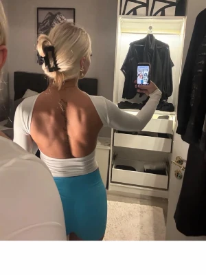 Vit långärmad topp med öppen rygg - Säljer en vit, tight långärmad topp med öppen rygg och rund halsringning. Toppen är croppad och har en stilren, minimalistisk look. Perfekt för dig som vill ha något trendigt och vågat. Materialet ser ut att vara stretchigt och mjukt.