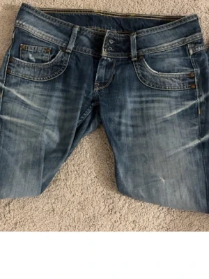 Mörkblå bootcut jeans från Pepe Jeans - Säljer ett par blå bootcut jeans från Pepe Jeans  med slitna detaljer och snygg tvätt. Jag skulle säga att det passar om man är mellan 34 och 36. De är väldigt lågmidjade så perfekt för någon som gillar det. Jättefina byxor, men kommer inte till användning.