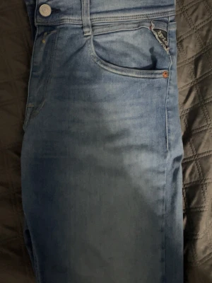 Blå raka jeans från replay - Säljer ett par klassiska blå jeans med raka ben och snygga slitningar framtill. Jeansen har fem fickor och en ljus tvätt som ger en avslappnad look. Perfekta till sneakers eller boots. Materialet är denim i bomull.