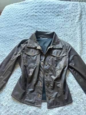 Brun skinnjacka från Maille Demoiselle - Snygg brun skinnjacka från Maille Demoiselle Paris med klassisk krage, två bröstfickor med lock och dekorativa sömmar. Jackan har knäppning framtill och figurnära passform som ger en fin look. Bak finns en spricka som bildats som jag försökte laga (se bild 3), inget som syns särskilt mycket. Det står inget stolek men passar som en XS och S. 