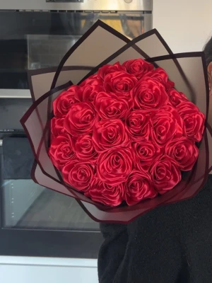 Bukett med röda konstgjorda rosor - Säljer en bukett med röda konstgjorda rosor i satinliknande material. Rosorna är tätt samlade och omslutna av svart och transparent inslagningspapper med dekorativ kant. Perfekt som present eller dekoration. Finns även likadana i färgen rosa. Antal rosor och pris kan diskuteras🌹🌸