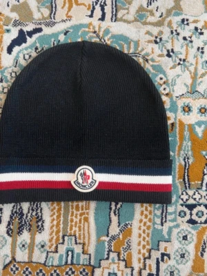 Svart Moncler mössa - Svart moncler mössa med blå och röd linjer. Den är helt ny aldrig använt och inga skador