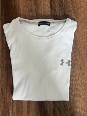 Vit t-shirt från Under Armour - Snygg vit t-shirt från Under Armour med klassisk rund hals och diskret logga på bröstet. Tillverkad i mjuk bomull som känns skön mot huden. 