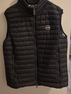 Svart dunväst från Colmar - Snygg svart dunväst från Colmar med quiltad design och hög krage. Västen har två dragkedjeförsedda fickor framtill och Colmar-logga på bröstet. Perfekt att slänga över en hoodie eller tröja för extra värme. Materialet är lätt och smidigt. Seriöst använt typ 6 gånger!