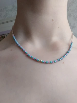 Pastellfärgat pärlhalsband - Sött halsband med små pärlor i pastellfärger, främst lila och turkos, samt några silvriga detaljer. Halsbandet har en tunn kedja i silverfärg och är perfekt för att ge en färgklick till din outfit. Ingen synlig logga eller märke.