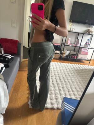 Olivgröna Juicy Couture mjukisbyxor - Säljer ett par olivgröna mjukisbyxor med raka ben och dragsko i midjan. Byxorna har stora fickor fram och bak, samt knappdetaljer på bakfickorna. Perfekta för en chill och avslappnad stil.