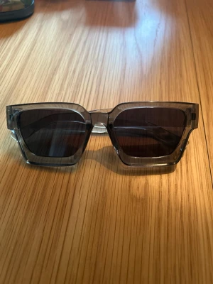 Svarta fyrkantiga solglasögon - Snygga solglasögon med bred, fyrkantig båge i transparent svart plast och mörka glas. Perfekta för dig som vill sticka ut med en trendig och modern look. Passar till alla tillfällen när solen skiner.