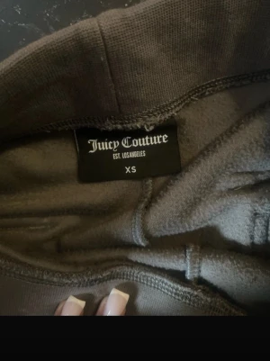 Grå hoodie från Juicy Couture XS - Mjuk och skön grå hoodie från Juicy Couture i storlek XS. Hoodien har dragkedja framtill, huva med snörning och är tillverkad i ett lent velourmaterial. Perfekt för en chill och avslappnad stil.