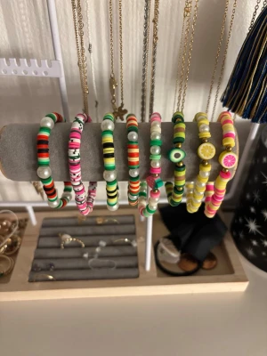 Sommar pärlarmband - Säljer flera handgjorda armband med färgglada plastpärlor i olika mönster och former. Armbanden har inslag av vita, gröna, rosa, gula och svarta pärlor samt detaljer som citron- och limepärlor.