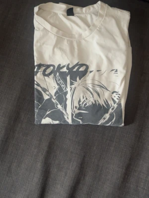 Vit Tokyo Ghoul långärmad tröja - Säljer en vit långärmad tröja med svart tryck från anime-serien Tokyo Ghoul. Framsidan har en stor grafisk illustration av en karaktär och texten 'TOKYO'. Perfekt för cosplay eller animefans som vill sticka ut med sin stil.
