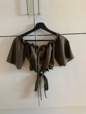 Grön offshoulder croppad topp - Grön offshoulder topp med korta ärmar. Har knytband i midjan för en justerbar passform. 