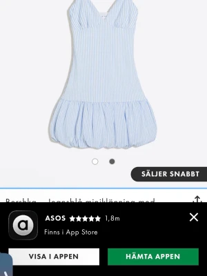 Blåvit randig kortklänning Bershka - Söt blåvit kortklänning från Bershka med tunna axelband och v-ringad hals. Klänningen har ett randigt mönster och en volangig kjoldel som ger en luftig känsla. Perfekt för varma dagar och enkel att styla med sneakers eller sandaler.