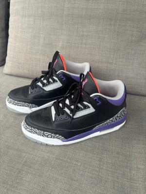 Air Jordan 3 svart/lila sneakers - Säljer ett par Air Jordan 3 sneakers använt en gång i svart läder med lila och orange detaljer. Skorna har klassiskt elephant print runt tån och hälen, vita och grå meshpaneler samt svart snörning. Snygg kontrast mellan färgerna och ikonisk siluett som alltid sticker ut.