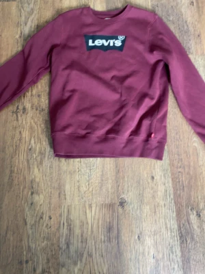 Vinröd sweatshirt från Levi's - Snygg vinröd sweatshirt från Levi's med klassisk logga på bröstet. Tröjan har rund halsringning, långa ärmar och ribbade muddar vid ärmslut och nederkant. Perfekt för en avslappnad och trendig look.