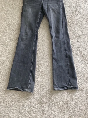 Grå bootcut jeans med slitna detaljer - Säljer ett par grå bootcut jeans med lätt slitna detaljer vid bensluten. Jeansen har klassisk femficksdesign och är tillverkade i mjukt denimtyg. Perfekta för dig som gillar en avslappnad och trendig look.