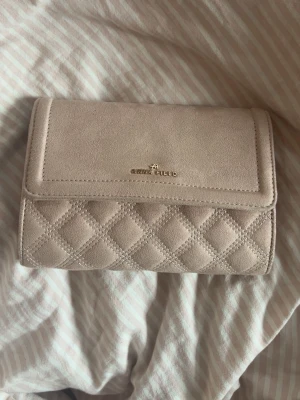 Beige quiltad handväska från Anna Field - Snygg beige handväska från Anna Field i mockaimitation. Väskan har quiltad design med rutmönster och guldfärgad logga på framsidan. Perfekt storlek för det viktigaste och stilren look som passar till många outfits.