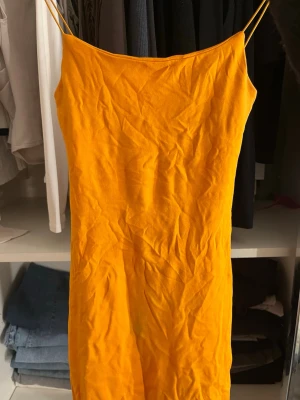 Orange klänning från Zara - Säljer en snygg orange klänning från Zara med smala axelband och rak passform. Klänningen är ärmlös och har en enkel, stilren design som gör den lätt att styla. Perfekt för varma dagar och somriga tillfällen.