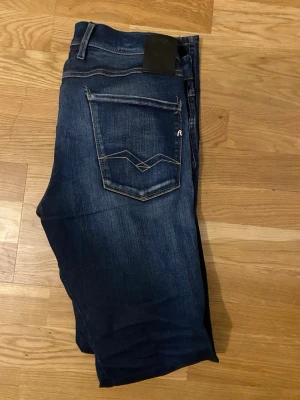 Mörkblå jeans från Replay - Säljer ett par mörkblå jeans från Replay med klassisk femficksdesign och snygga kontrastsömmar på bakfickorna. Jeansen har en rak passform och är tillverkade i slitstark denim med lätt tvättad effekt. Perfekta för en avslappnad och trendig look.