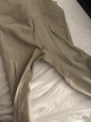 Beige ribbade leggings från Bik Bok - Säljer ett par beige ribbade leggings från Bik Bok i storlek M. De har hög midja och är tillverkade i ett stretchigt, mjukt material som sitter skönt på kroppen. Perfekta för en avslappnad och trendig look.