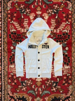 *RARE* eftertraktad hollister hoodie ~ 2000-tal - Snygg vit hoodie från Hollister med stora svarta knappar framtill och tryckt logga över bröstet. Hoodien har huva, två fickor och ribbade muddar vid ärmar och nederkant. Perfekt för en chill och avslappnad stil.