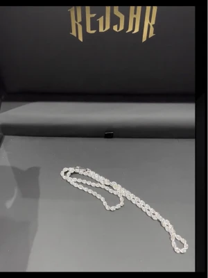 Silverfärgat repkedje-halsband Kejsar - Säljer ett stilrent halsband från Kejsar med repkedje-design i silverfärg. Halsbandet har en tvinnad form som ger en exklusiv känsla och passar perfekt till dig som gillar att sticka ut med accessoarer. Materialet ser ut att vara metall med glansig finish.