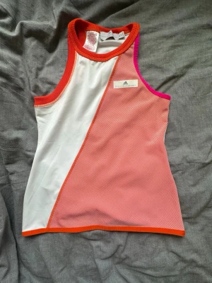 Adidas Stella McCartney sportset - Säljer ett sportigt set från Adidas Stella McCartney med ett linne i vitt med orange och rosa detaljer samt en vit kjol Perfekt för tennis eller träning, köp båda för 300 eller 200 kr styck. Linne i storlek 152 som motsvarar XS, sedan kjolen i storlek 36. Använt setet en gång. 