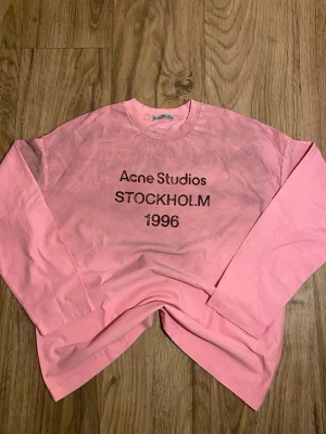 Rosa långärmad tröja Acne Studios - Säljer en rosa långärmad tröja från Acne Studios med tryck 'STOCKHOLM 1996' på bröstet. Tröjan har en avslappnad passform och är tillverkad i mjuk bomull. Perfekt för dig som gillar streetwear och vill ha något stilrent men ändå statement.