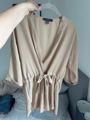 lång beige blus med knytning  - säljer en blus som är lång till lite nedanför höfterna.