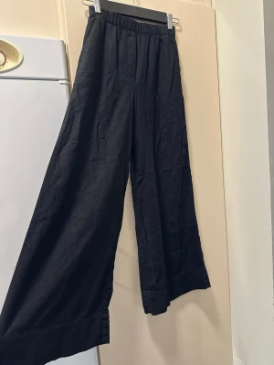 Svarta vida linnebyxor med resår - Säljer ett par svarta linnebyxor med breda ben och resår i midjan. Byxorna har en avslappnad passform och är tillverkade i ett svalt linnematerial, perfekta för en chill och stilren look. Har fickor men inga bakfickor bara detalj. Aldrig använd och helt ny! OBS: FRAKTAR INOM 24H!🩷