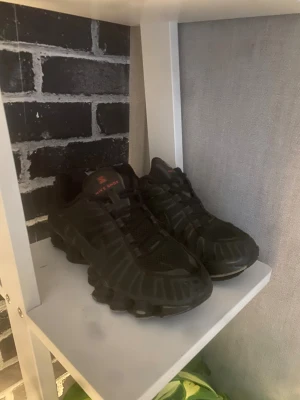 Nike Shox svarta sneakers - Nike Shox sneakers i helsvart med röda detaljer på plösen. Skorna har en sportig design med mesh och syntetmaterial, samt den ikoniska Shox-sulan som ger extra studs och cool look. Perfekta för dig som gillar streetwear och vill sticka ut med en unik siluett. De är lite uppskrapade på fram sidan men inget som försämrar själva skorna