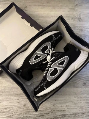 Svarta sneakers från Axel Arigato - Svarta skor från Cristian Dior med vita och grå detaljer samt vita snören. Perfekta om du vill uppdatera din stil. Skorna har inga skador och är 10/10 skick. Dm vid fler frågor eller funderingar