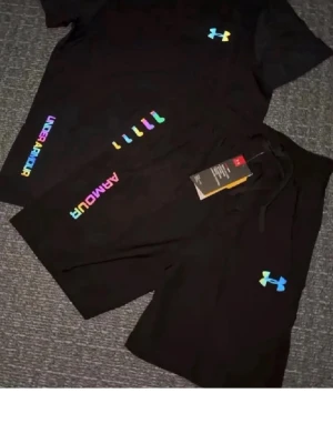 Svarta shorts från Under Armour - Säljer ett par svarta shorts från Under Armour med färgglad logga och text på benet. Shortsen har snörning i midjan och är perfekta för träning eller chill. Materialet känns mjukt och lätt, vilket gör dem sköna att bära under varma dagar.