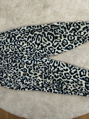 Leopardmönstrade leggings i blått och svart - Snygga leggings med leopardmönster i svart och blått på ljus bakgrund. Mjukt och stretchigt material som sitter skönt. Perfekta för dig som vill sticka ut med ett coolt mönster. Midjemodell med resår för bästa passform.