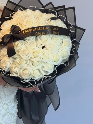 Bukett med vita rosor och svart band - Snygg bukett med vita konstgjorda rosor, dekorerad med ett svart band med texten 'Congratulations Class of 2026' och pärlband runt om. Insvept i svart cellofan och stor rosett. Perfekt som present till examen eller firande.