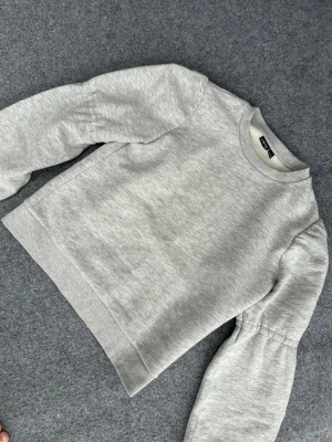 Grå sweatshirt med puffärm LMTD - Ljusgrå sweatshirt från LmTD med puffärmar och rund halsringning. Tillverkad i jättemjukt mjukt sweatshirtmaterial och har ribbade muddar vid ärmslut och nederkant. Enkel och trendig modell som ger en avslappnad look.
