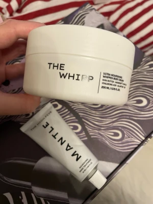 MANTLE The Whipp & The High Five hand cream  - Säljer ett kit från MANTLE med The Whipp ultra-nourishing whipped body cream (200 ml) och The High Five nourishing hand treatment (50 ml). Båda i stilrena vita förpackningar, med sheasmör, hyaluronsyra och vårdande ingredienser för mjuk hud.