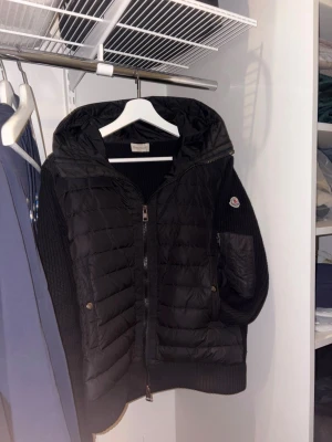 Svart dunjacka med luva huva från Moncler - Snygg svart dunjacka från Moncler med stickade ärmar och vadderad kropp. Jackan har dragkedja framtill, huva och en ficka med Moncler-logga på ärmen. NFC finns. Bara skriva om du har några frågor💯pris kan diskuteras vid snabb köp 🙏🏻